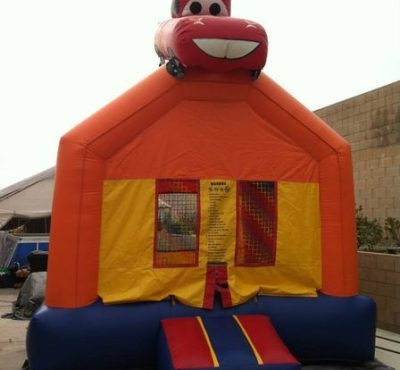A colorful bounce house with a toy car perched on top, set against a clear blue sky.